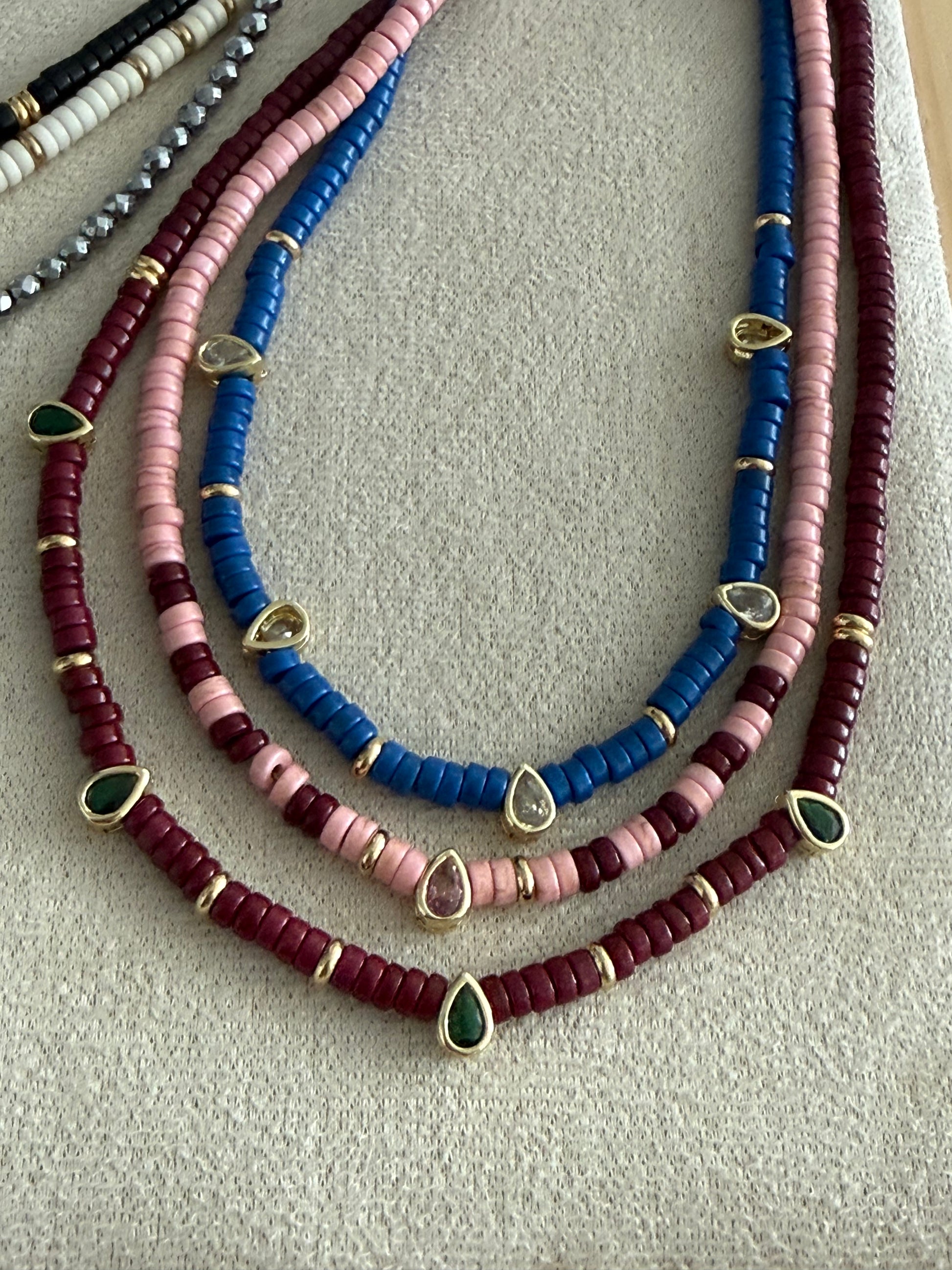 Three beaded necklaces in blue, pink, and red on a textured surface